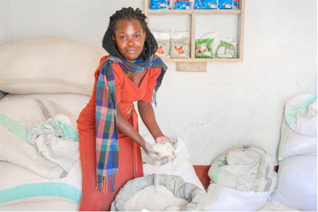 Winnie Kiiza holds animal feed beside sacks of feed.