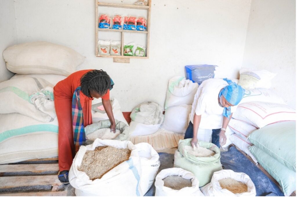 Winnie Kiiza and another woman work with open sacks of animal feed.