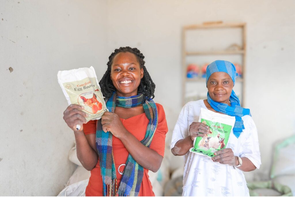 Winnie Kiiza and another woman display packaged poultry feed products.