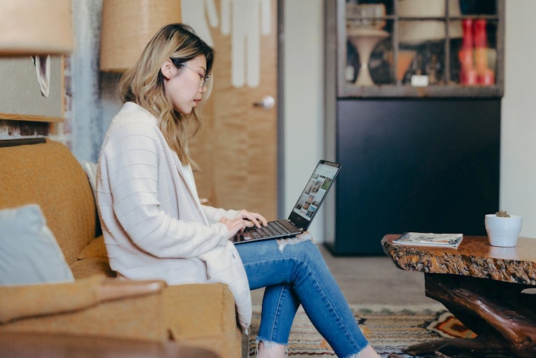 Woman on couch searching on laptop.